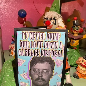May include: A black card with a white and blue geometric pattern background. The card has the text "I'd never dump our love down a garbage disposal" in white letters. A black and white photo of a man with glasses and a mustache is in the center of the card.