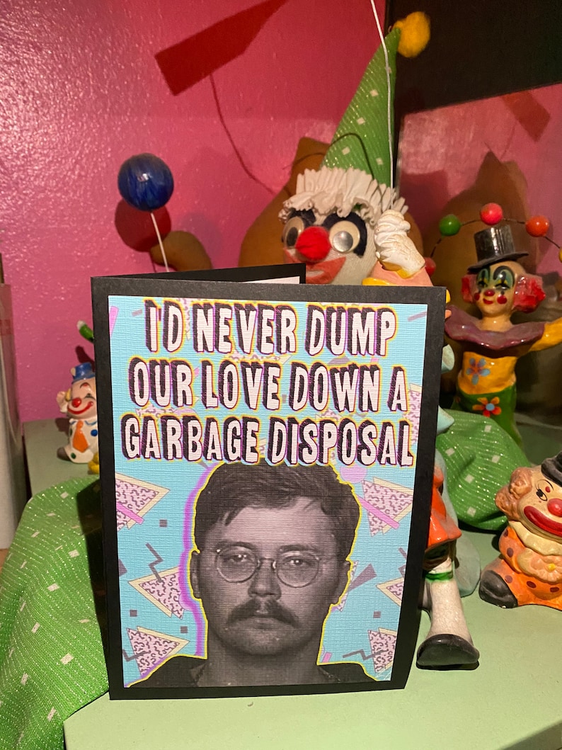 May include: A black card with a white and blue geometric pattern background. The card has the text "I'd never dump our love down a garbage disposal" in white letters. A black and white photo of a man with glasses and a mustache is in the center of the card.