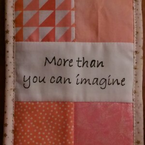May include: A pink and orange quilted wall hanging with the text "More than you can imagine" embroidered in black thread.
