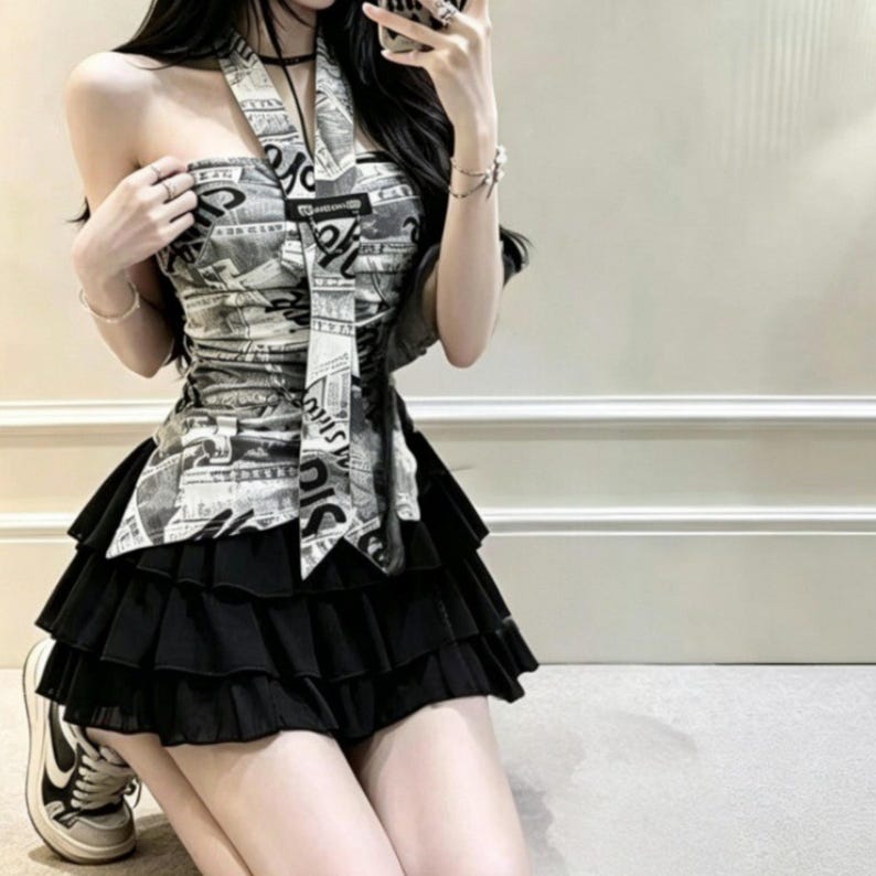 Puede incluir: Un top de cuello halter con estampado de peri&oacute;dico en blanco y negro y un detalle de lazo central, combinado con una minifalda negra compuesta por varias capas de volantes horizontales. El conjunto se lleva con zapatillas deportivas.