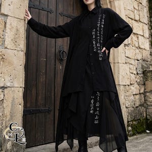 May include: A long-sleeved black button-down shirt featuring white Asian character text on the chest and a layered, asymmetrical skirt with matching white text. The garment has a flowing, multi-layered hemline with sheer fabric panels.