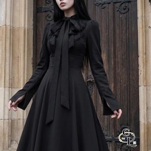 May include: A black dress with a high collar and a flowing skirt. The dress has long sleeves with split cuffs and a large bow at the neckline. The dress is made of a soft, flowing fabric.