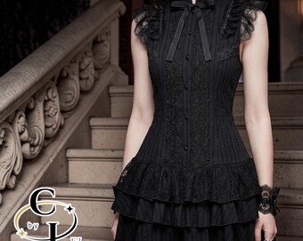 Puede incluir: Vestido negro sin mangas con cuello alto y falda escalonada. El vestido presenta detalles de encaje en el corpiño, los hombros y la falda. Un lazo negro adorna el escote. El vestido se lleva con un brazalete negro. El logotipo de la marca es visible.