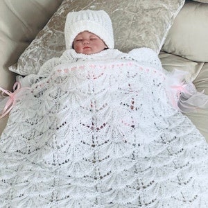 May include: A white crocheted baby blanket with a delicate lace pattern. A baby is wearing a white crocheted hat and is wrapped in the blanket.