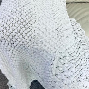 May include: White crocheted baby blanket with a delicate lace border and a textured pattern.