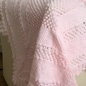 Puede incluir: Una manta de bebé de ganchillo rosa con un delicado borde de encaje. La manta está hecha con un hilo suave y ligero, perfecto para acurrucarse.