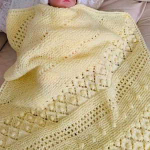 Könnte beinhalten: Eine gelbe gestrickte Babydecke mit einem zarten Stichmuster und kleinen Noppen. Die Decke ist weich und kuschelig, perfekt für ein Neugeborenes.