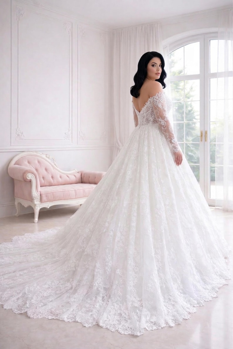 Peut inclure: Une robe de mari&eacute;e blanche &agrave; &eacute;paules d&eacute;nud&eacute;es avec des manches longues en dentelle et une jupe ample arrivant au sol, dot&eacute;e d'une longue tra&icirc;ne. Le corsage et les manches sont orn&eacute;s de broderies florales en dentelle complexe.