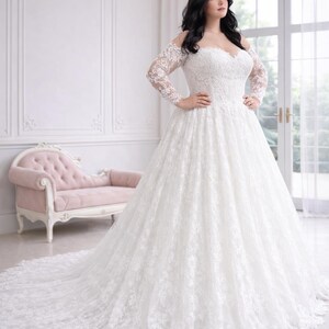 Peut inclure: Une robe de mari&eacute;e blanche longue jusqu'au sol avec une encolure d&eacute;gag&eacute;e, des manches longues en dentelle et un corsage en forme de c&oelig;ur. La robe est orn&eacute;e de superpositions de dentelle florale complexe sur le corsage et la jupe volumineuse.