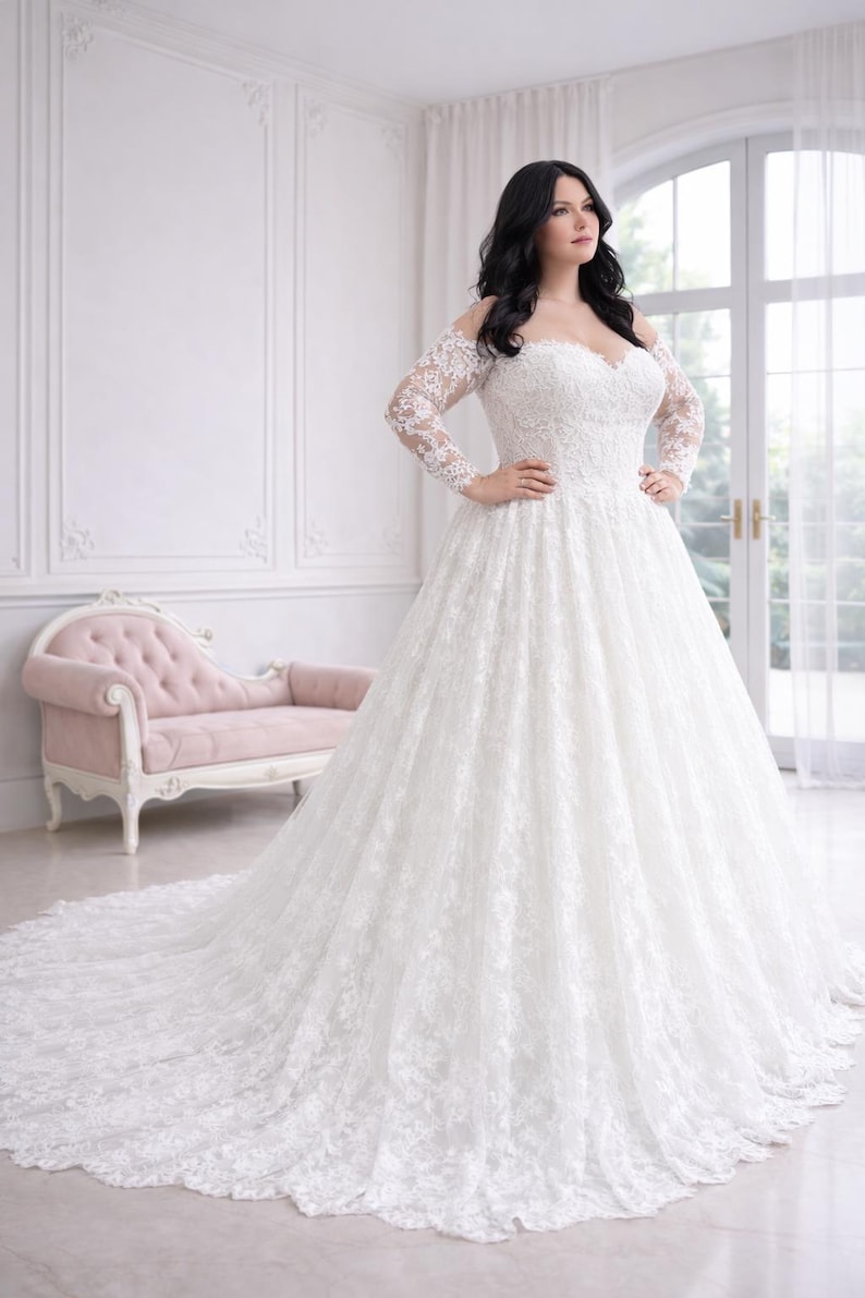 Peut inclure: Une robe de mari&eacute;e blanche longue jusqu'au sol avec une encolure d&eacute;gag&eacute;e, des manches longues en dentelle et un corsage en forme de c&oelig;ur. La robe est orn&eacute;e de superpositions de dentelle florale complexe sur le corsage et la jupe volumineuse.