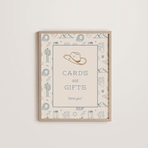 May include: A beige sign with a brown frame and a blue and white pattern of cacti, stars, and cowboy hats. The sign says "Cards and Gifts, thank you!" with a cowboy hat graphic above the text.
