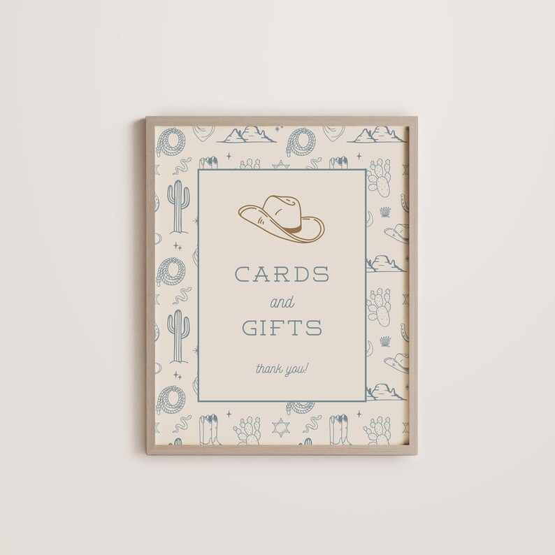 May include: A beige sign with a brown frame and a blue and white pattern of cacti, stars, and cowboy hats. The sign says "Cards and Gifts, thank you!" with a cowboy hat graphic above the text.