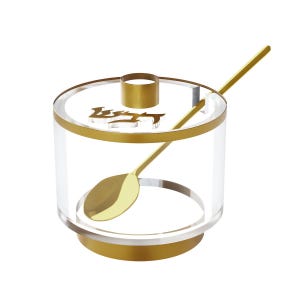 May include: Clear acrylic sugar bowl with gold-colored accents, including a rim, base, and spoon. The lid features a gold handle and an inscription. The spoon rests inside the bowl, ready for use.