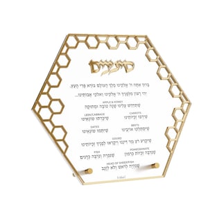 May include: A gold-colored, hexagonal-shaped decorative sign with a honeycomb design around the edges. The sign features Hebrew text and lists various foods. The sign is designed to stand upright.