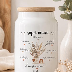 Pode incluir: Um pote de cerâmica branca com tampa de madeira clara, apresentando um gráfico impresso de um buquê de flores secas em um pequeno vaso. O texto diz: super nounou, Merci pour, ton écoute, tes câlins réconfortants, ta douceur, ta bienveillance, ta patience, ta bonne humeur, et bien plus encore, Arthur.