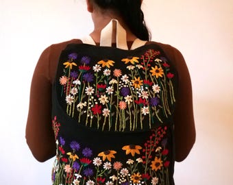 May include: Black canvas backpack with a floral embroidery design. The embroidery features a variety of colorful flowers and leaves.
