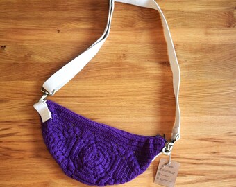 Sac banane violet crocheté à la main en laine certifiée GOTS ; son achat soutient un projet pour les femmes en Inde.