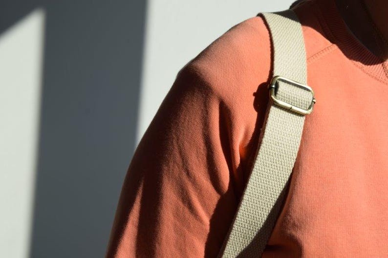 Pode incluir: Um close-up de uma pessoa vestindo uma camisa cor coral com uma al&ccedil;a de lona bege. A al&ccedil;a tem uma fivela de lat&atilde;o.