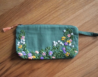 Trousse à maquillage verte brodée à la main, issue d'une production équitable, ornée de broderies florales en ruban de soie, fabriquée en coton biologique certifié GOTS.
