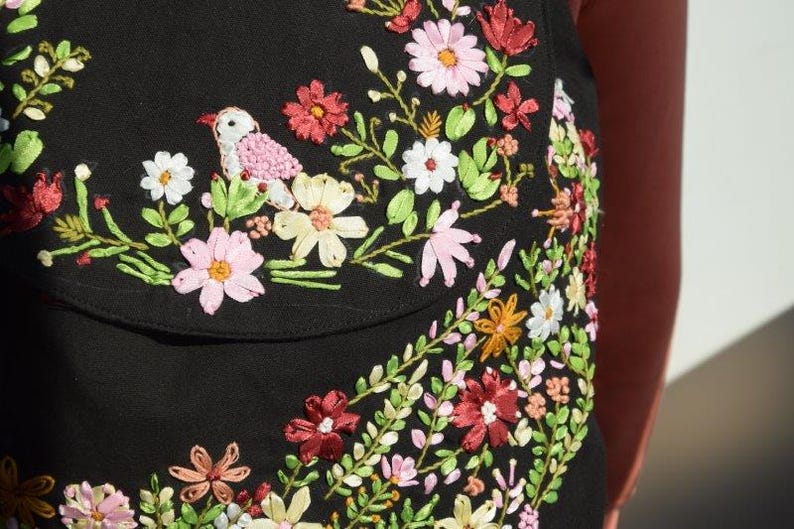 Pode incluir: Tecido preto com flores bordadas coloridas e um pequeno p&aacute;ssaro. O bordado &eacute; feito com fita e fio.