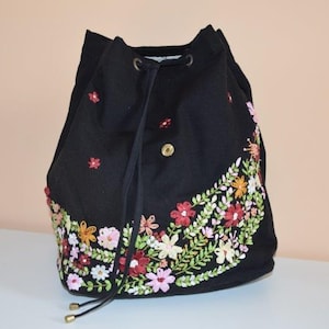 Pode incluir: Saco preto de cord&atilde;o com um design de bordado floral em tons de rosa, verde e amarelo.