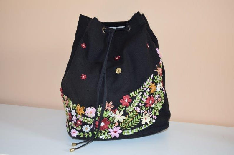 Pode incluir: Saco preto de cord&atilde;o com um design de bordado floral em tons de rosa, verde e amarelo.