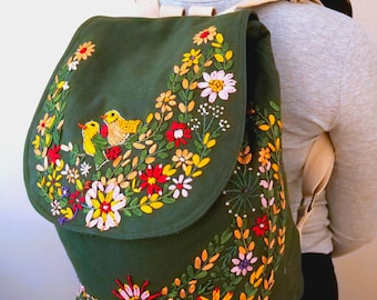 May include: A green canvas backpack with embroidered flowers and birds in shades of yellow, red, pink, and white.