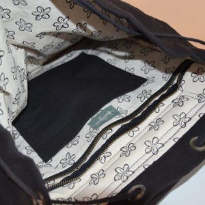 May include: Black drawstring backpack with a white floral patterned lining. The interior features a zippered pocket and a large open space. The bag has a drawstring closure and metal eyelets.