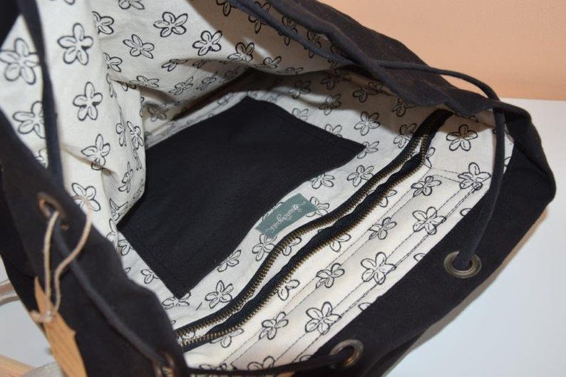May include: Black drawstring backpack with a white floral patterned lining. The interior features a zippered pocket and a large open space. The bag has a drawstring closure and metal eyelets.