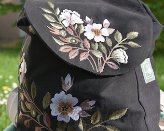 Sac à dos fait main en toile noire avec broderie de roses sauvages, fabriqué en coton biologique certifié GOTS et issu du commerce équitable. Soutient un projet d'ONG pour les femmes en Inde.