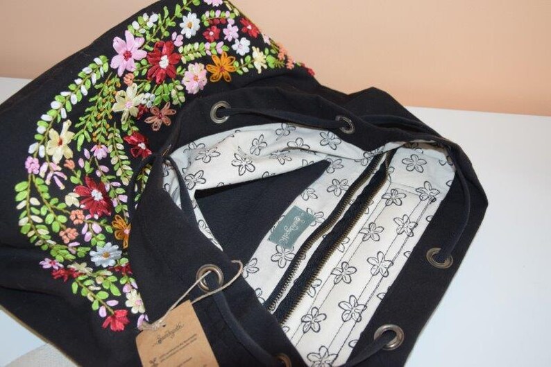 Pode incluir: Sacola tote de lona preta com um design de bordado floral. A bolsa tem fecho de correr e um topo com cord&atilde;o.