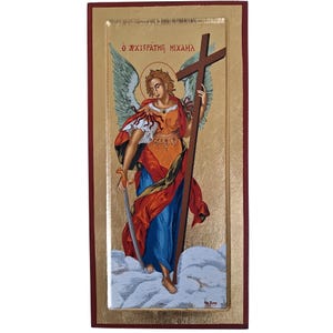 Puede incluir: Un icono religioso rectangular sobre fondo dorado que muestra a un ángel con alas, vestido con una túnica roja y azul, sosteniendo una gran cruz de madera marrón y una espada. El texto griego O ARCHISTRATEGOS MICHAIL aparece en la parte superior.