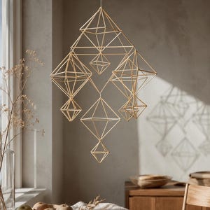 May include: A hanging geometric mobile constructed from thin, light-colored straw or reed segments. The structure consists of multiple interconnected diamond and pyramid shapes suspended by a single thin thread, creating a complex, airy, three-dimensional lattice design.