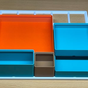 May include: A white organiser tray with four removable compartments. The compartments are in different colours: orange, teal, brown, and teal.