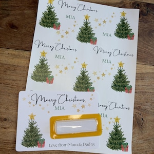 May include: Christmas-themed gift tags and labels. The design features watercolor illustrations of Christmas trees, gift boxes, and gold stars. The text includes "Merry Christmas" and "MIA". A label with a yellow border is also included.