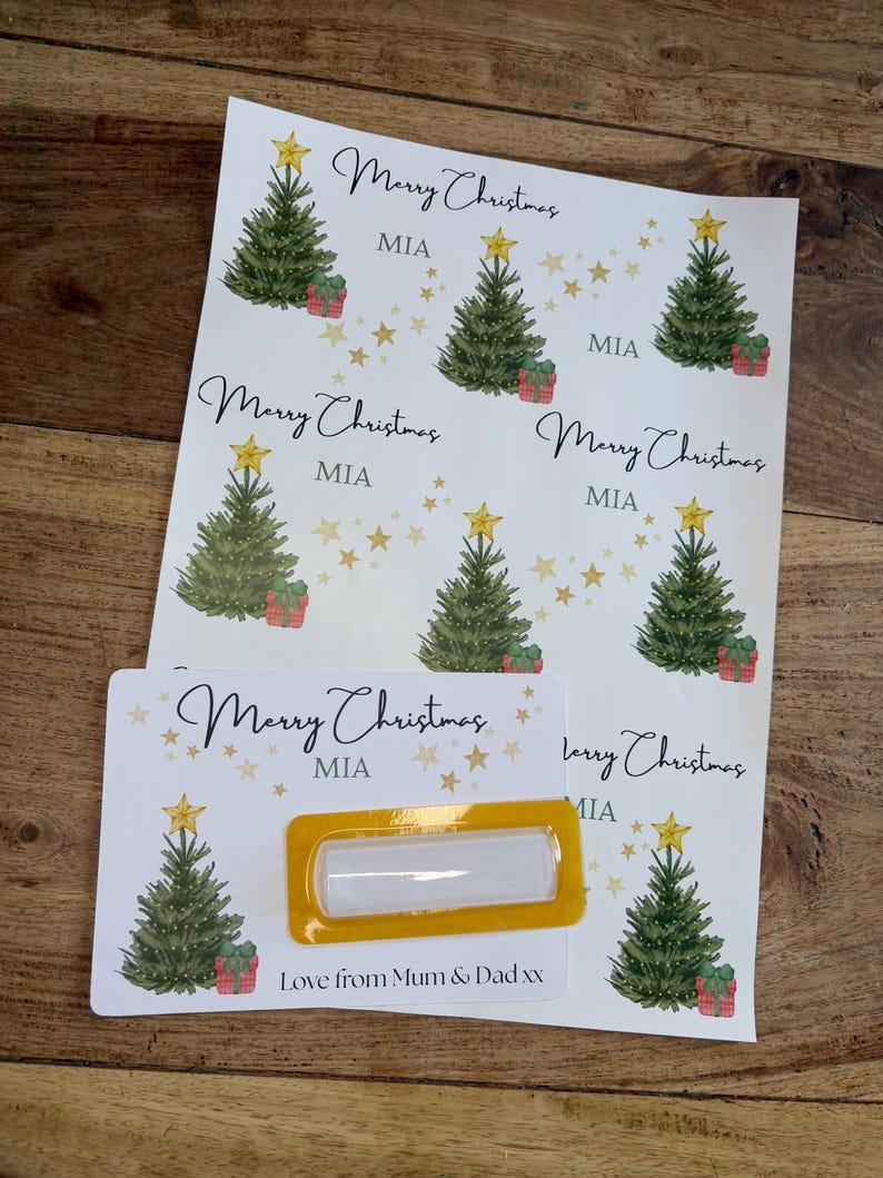 May include: Christmas-themed gift tags and labels. The design features watercolor illustrations of Christmas trees, gift boxes, and gold stars. The text includes "Merry Christmas" and "MIA". A label with a yellow border is also included.