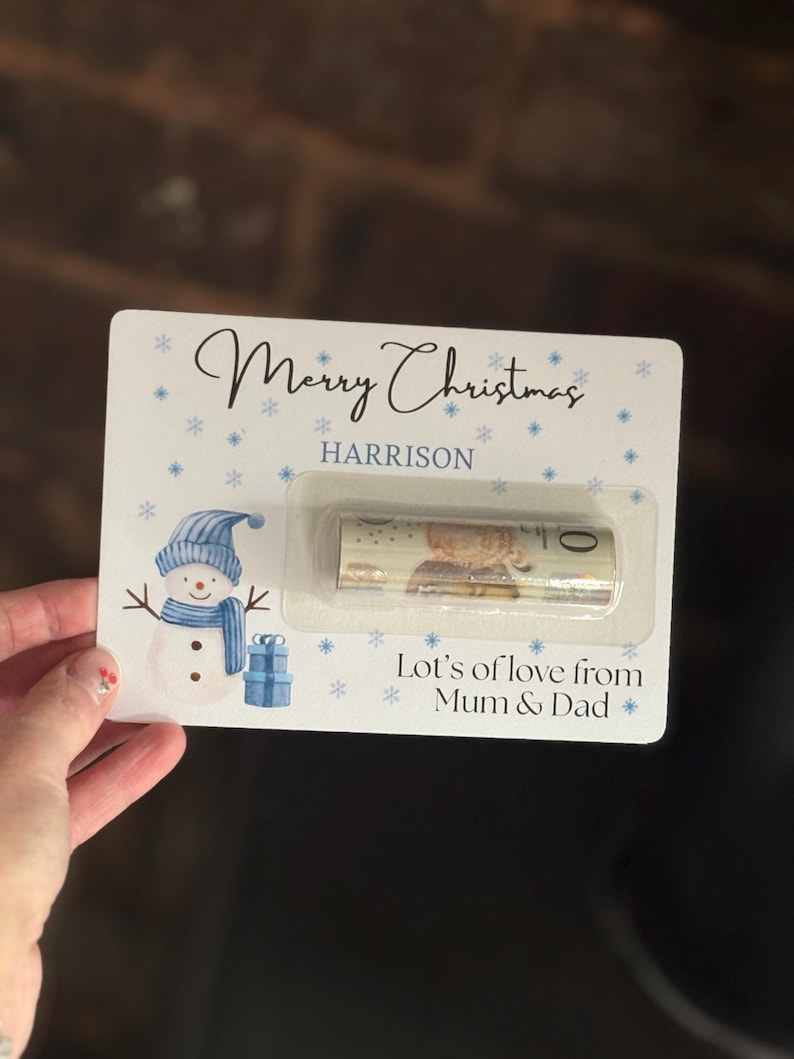May include: A Christmas gift card with a snowman illustration, snowflakes, and the text "Merry Christmas HARRISON". The card includes a rolled-up bill in a clear plastic holder, with the message "Lot's of love from Mum & Dad".