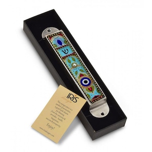 May include: A mezuzah with a blue and white enamel design featuring a hamsa hand, an evil eye, and Hebrew lettering. The mezuzah is in a black box with a gold label that reads "IRIS Design".