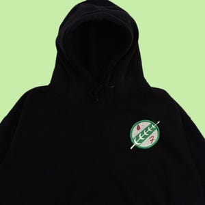 Puede incluir: Sudadera con capucha negra con un parche bordado verde y rojo del s&iacute;mbolo de la Alianza Rebelde de Star Wars.