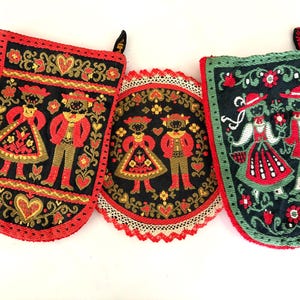 Puede incluir: Tres accesorios de cocina de tela con bordados de figuras con vestimenta tradicional. Dos piezas rectangulares tienen bordes rojos, mientras que la pieza circular central tiene un borde de encaje blanco festoneado. Todos los artículos muestran fondos negros con motivos florales.