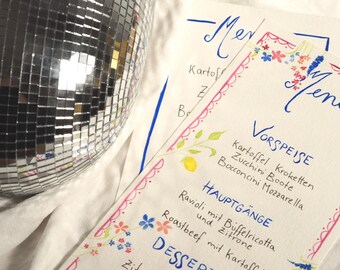 May include: A handwritten menu with a pink and blue floral border. The menu is titled "Menu" and lists the following items: Vorspeise (Appetizer), Kartoffel Kroketten (Potato Croquettes), Zucchini Boote (Zucchini Boats), Bocconcini Mozzarella, Hauptgänge (Main Courses), Ravioli mit Büffelricotta (Ravioli with Buffalo Ricotta), Roastbeef mit Kartoffel und Zitrone (Roast Beef with Potatoes and Lemon), Dessert (Dessert), and Zitrone (Lemon).