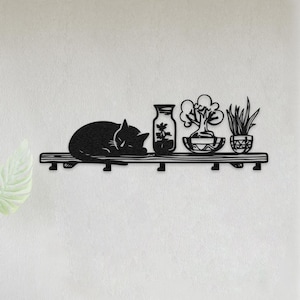 May include: Black metal wall art depicting a sleeping cat on a shelf with decorative plants in vases and pots. The shelf is mounted on a white wall near a white door. The cat is curled up, and the plants are stylized.