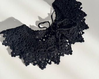 May include: A black crocheted collar with a delicate lace pattern. The collar is tied at the back with a ribbon.