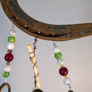 May include: A rustic horseshoe wind chime with beads in shades of red, white, and green. The beads are strung on wire and hang from the horseshoe. There is a small bone charm hanging from the horseshoe.