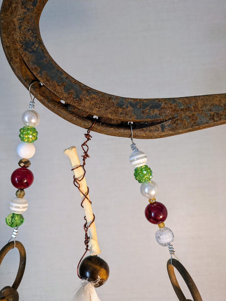 May include: A rustic horseshoe wind chime with beads in shades of red, white, and green. The beads are strung on wire and hang from the horseshoe. There is a small bone charm hanging from the horseshoe.
