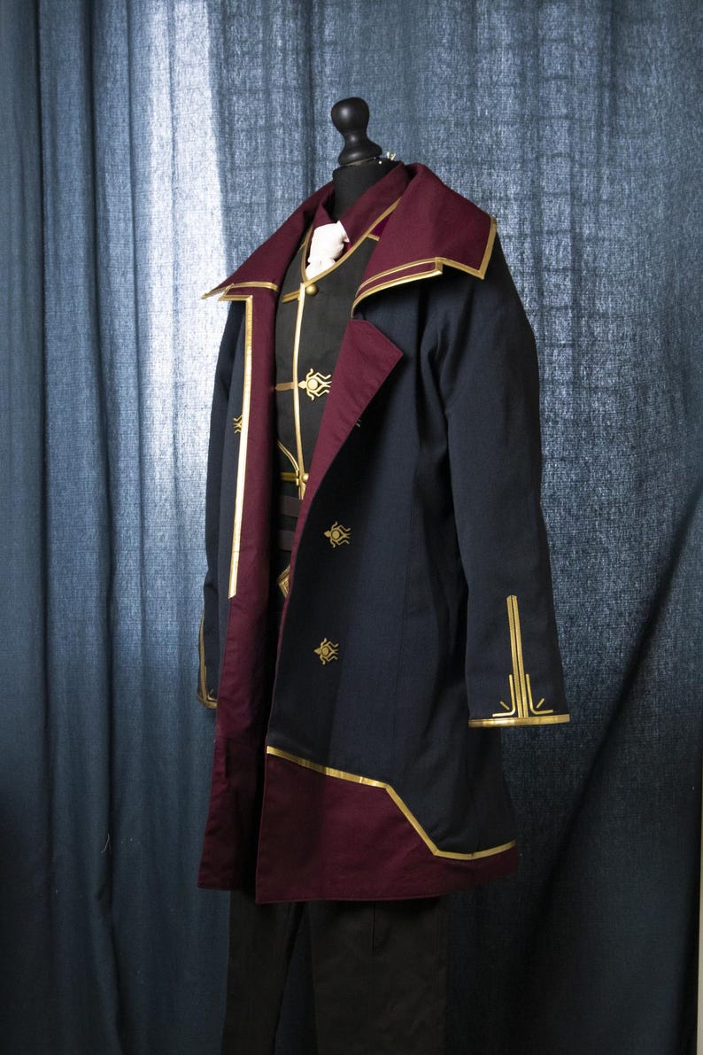 May include: A dark blue coat with a burgundy lining and gold trim. The coat has a high collar and a single button closure. The coat is decorated with gold embroidery.
