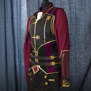 May include: A black and burgundy vest with gold accents and a matching burgundy sleeve cuff. The vest has a decorative design with a gold trim and a belt with gold buckles. The sleeve cuff has a floral design.