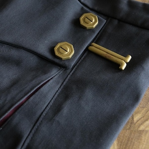 May include: Close-up of a dark blue fabric with two gold buttons and a gold metal clasp. The fabric has a subtle texture and a slight sheen.