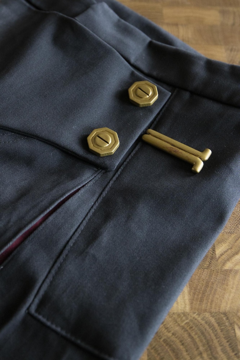 May include: Close-up of a dark blue fabric with two gold buttons and a gold metal clasp. The fabric has a subtle texture and a slight sheen.