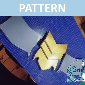 Könnte beinhalten: Ein Schnittmuster für ein Kostümteil, bestehend aus zwei grauen Teilen und drei goldenen Teilen. Die Teile liegen auf einer blauen Schneidematte.